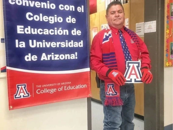 Jose Olivas in UA gear standing next to spanish language banner