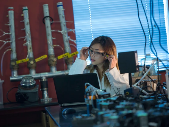 young woman sitting in a lab environment in a lab coat looking at laptop