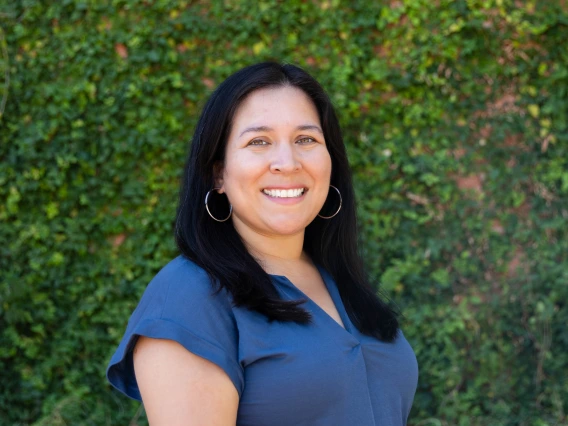 lopez headshot, wearing a blue blouse, greenery in the background