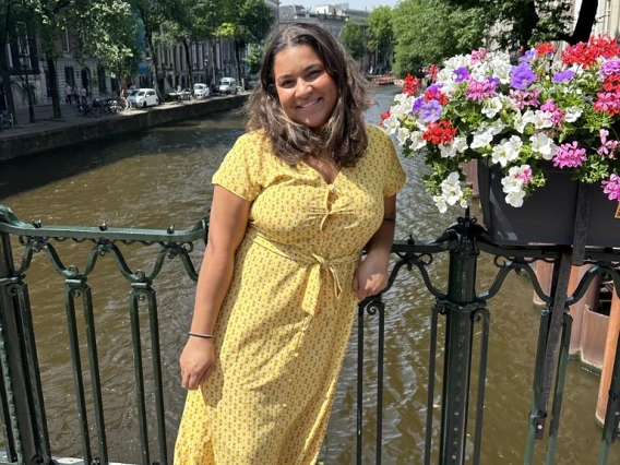 dominique washington in a yellow dress standing on a bridge with river as a backdrop 