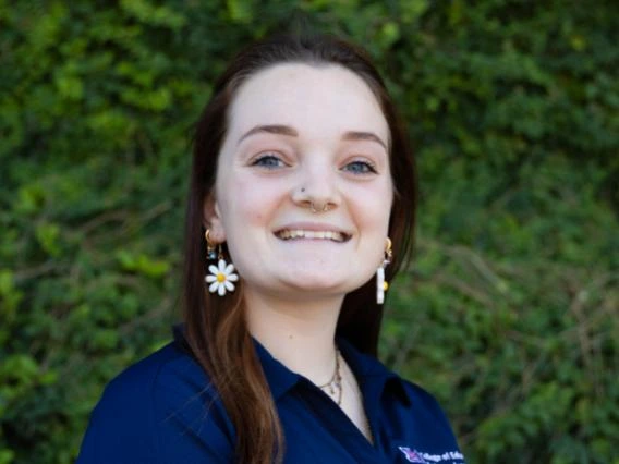 Kiersten Scarbrough wearing a blue polo shirt, reddish medium length hair, greenery in the background