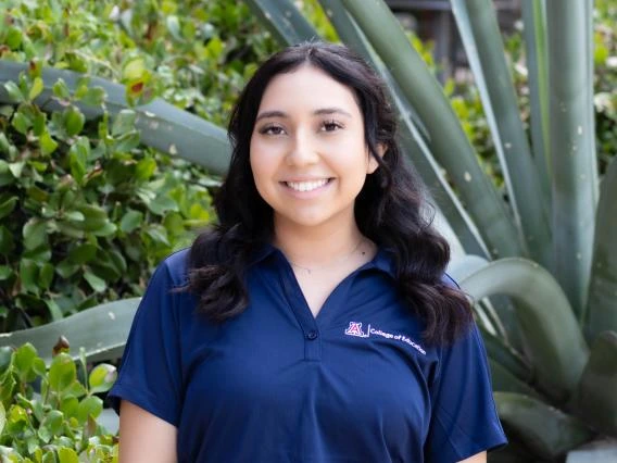 Sandy Servellon wearing a blue polo shirt, medium length dark hair, greenery in the background