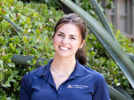 Roarke Poggio wearing a blue shirt, dark hair in a ponytail, greenery in the background