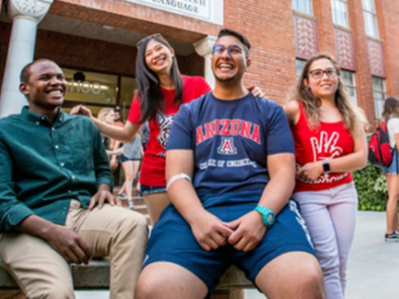 4 college students sitting outside conversing and smiling under a sunny sky