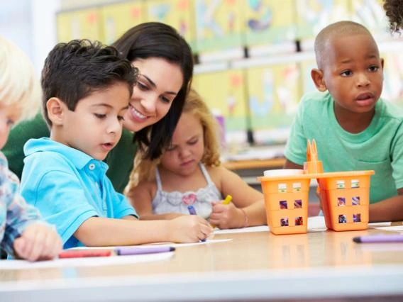 teacher with young students sitting around a table in school classroom setting