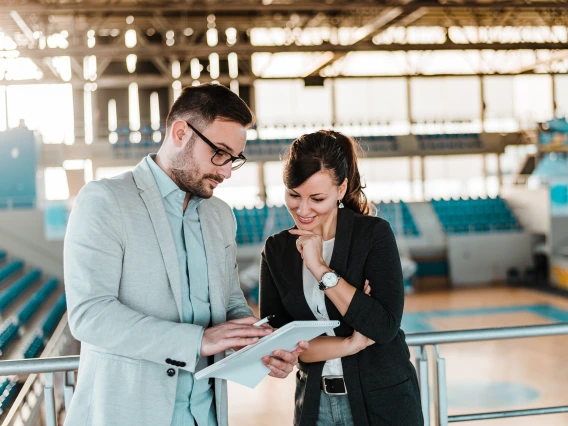 man and woman standing in a gym, talking to each other looking at a notepad