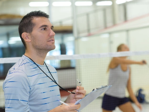 Man with whistle and clipboard in front of badminton net