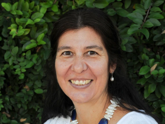 sara chavarria headshot, wearing a white blouse with greenery in the background