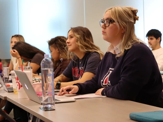 students sitting in a row at a table listening to a lecture