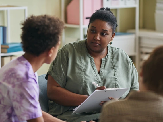 adult in green blouse speaking with two youths