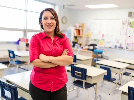 young teacher standing in classroom wearing a red blouse arms crossed