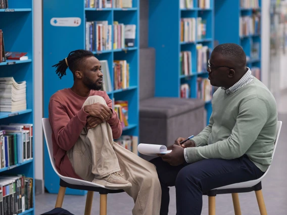 two men sitting in front a wall of books talking to each other