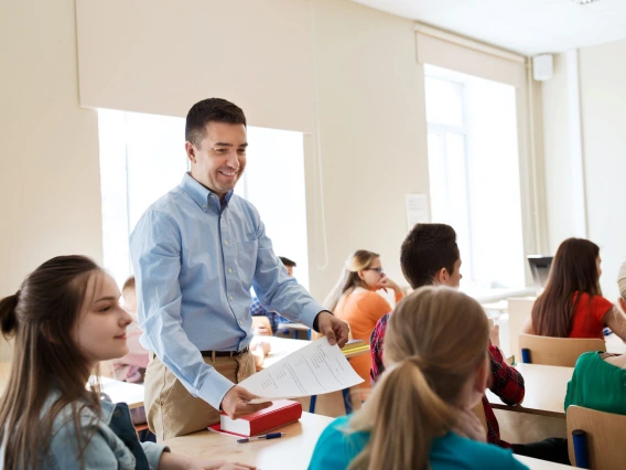 teacher standing in the aisle of a classroom looking at students sitting in their desks