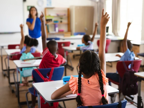 classroom of young students, raising their hands