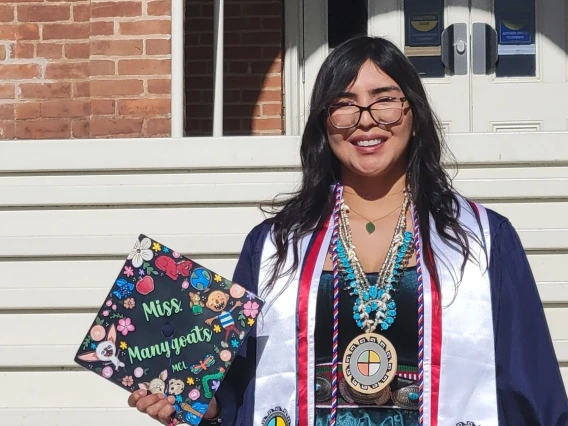 ITEP educator in graduation cap and gown on the steps of old main