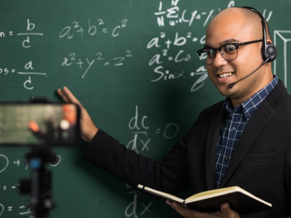 instructor wearing a headset standing at a blackboard while being filmed