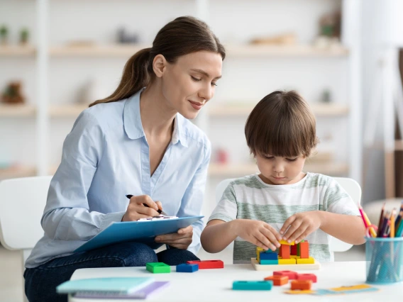 Assessment of kids mental development. Professional woman psychologist watching little boy playing with logical game