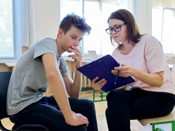 Woman school psychologist talking and helping student, male teenager