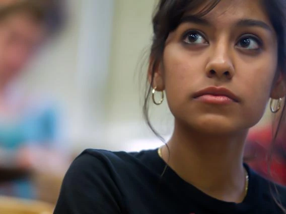 young student with dark hair pulled back in a bun, sitting in class listening