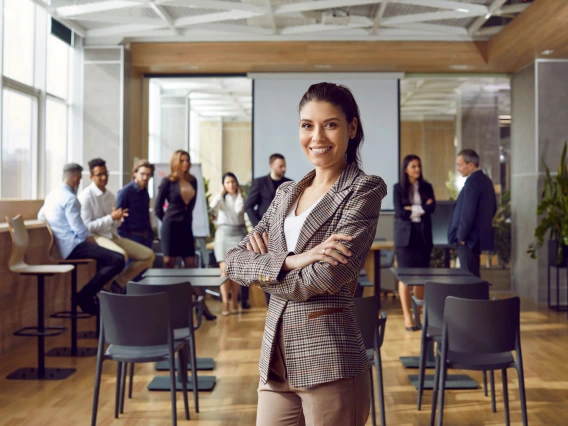 Happy professional business teacher after corporate training class for team of workers. Beautiful young woman in suit jacket standing in office conference room, looking at camera and smiling