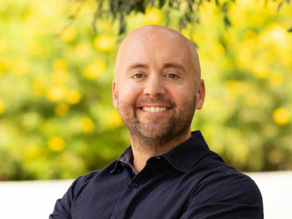 matt ostermeyer headshot, standing outside under a sunny sky, wearing a black polo, arms crossed