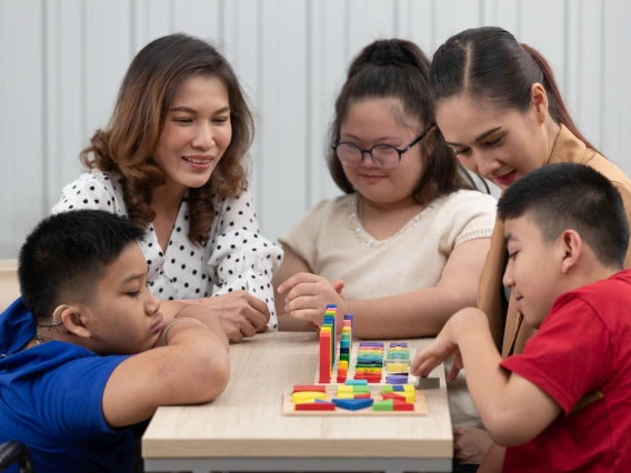 Group of special students in classroom, a down syndrome girl, two handicapped boys and cute Asian teacher playing toy and game together