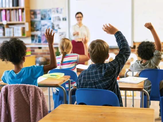 Education, question with group of children in classroom and raise their hands to answer. Learning or support, diversity and teacher teaching with young students in class of school building together