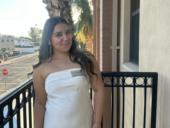 Alisa standing outdoors on a balcony wearing a white strapless dress