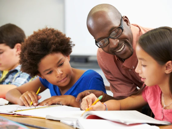 Teacher Helping Pupils Studying At Desks In Classroom