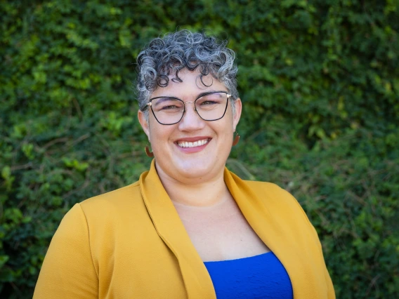 heather wearing yellow jacket, blue blouse, glasses and salt and pepper hair, greenery in background