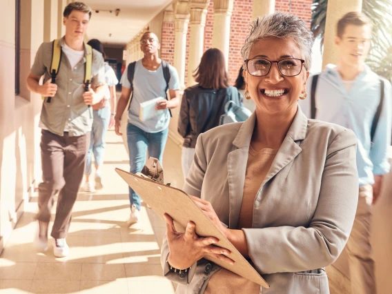 woman wearing glasses holding a clipboard and students in the distance walking with backpacks