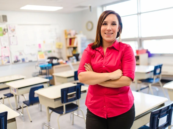 young teacher standing in classroom wearing a red blouse arms crossed