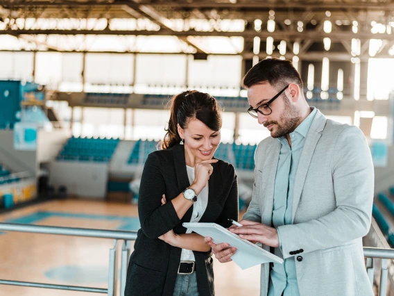 man and woman standing in a gym, talking to each other looking at a notepad