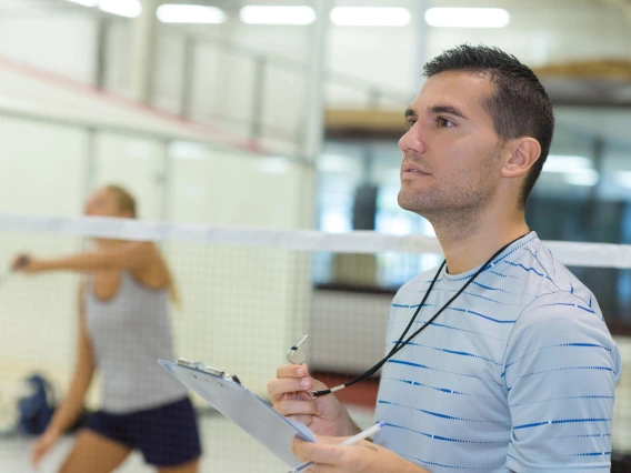 Man with whistle and clipboard in front of badminton net