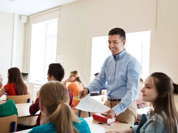 teacher standing in the aisle of a classroom looking at students sitting in their desks