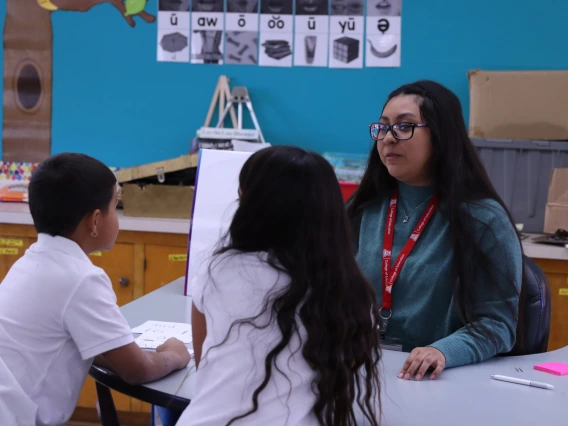 educator sitting at a table with two young students in a classroom