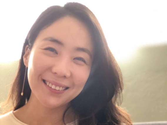 A warm and softly lit portrait of Dr. Sung Eun Jung smiling at the camera. She has long, dark hair and is wearing a cream-colored sweater with a delicate drop earring. 
