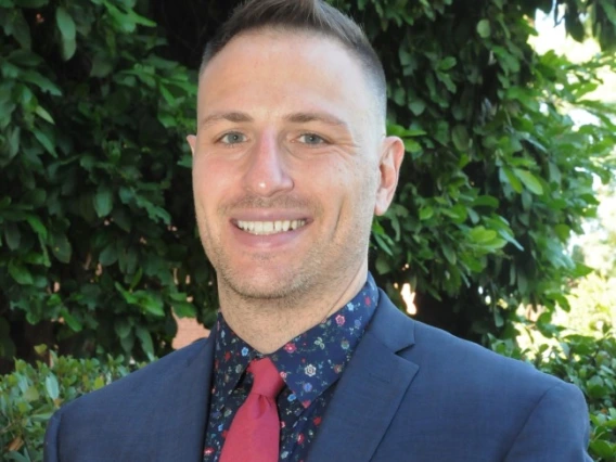 Dr. Jonathan Tullis smiling standing in front of greenery.