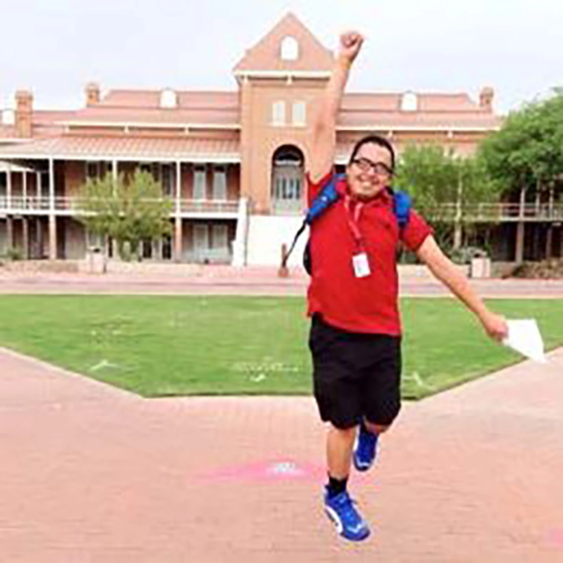 Student jumping up with a fist pump in front of old main