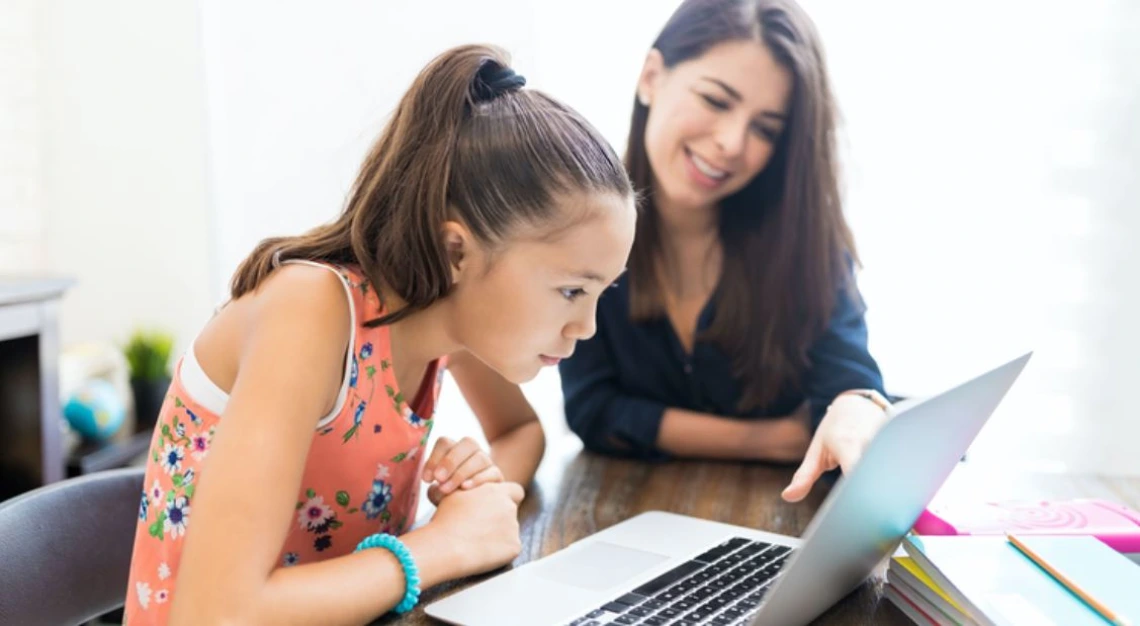 Young woman and child at table looking at laptop screen