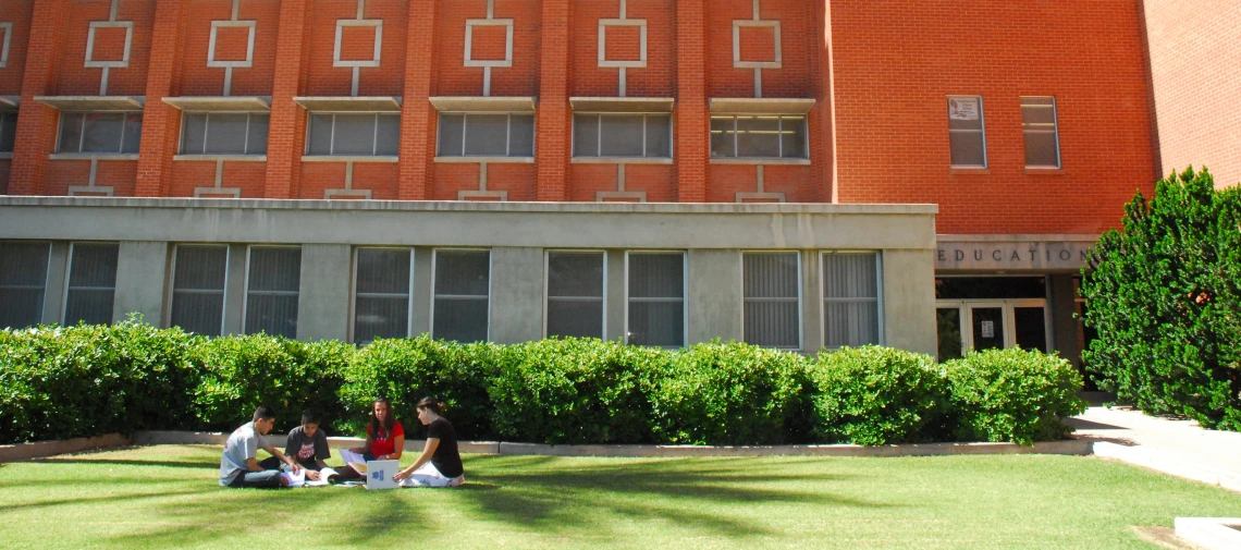 four students sitting on the lawn in front of the education building on a sunny day