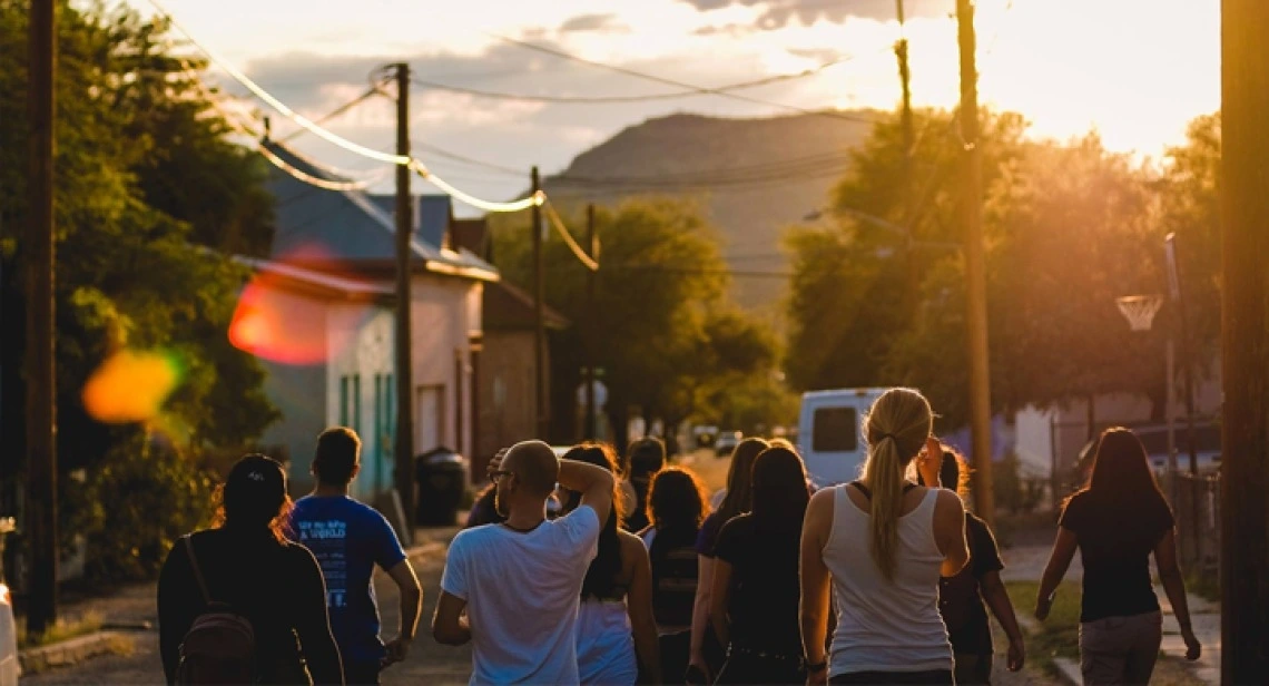 people walking in a street towards a sunset with a mountain in the distance