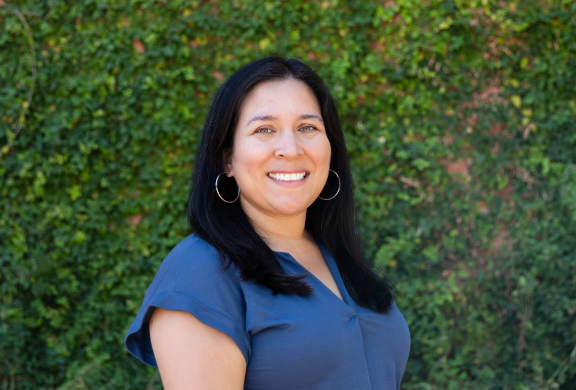 lopez headshot, wearing a blue blouse, greenery in the background