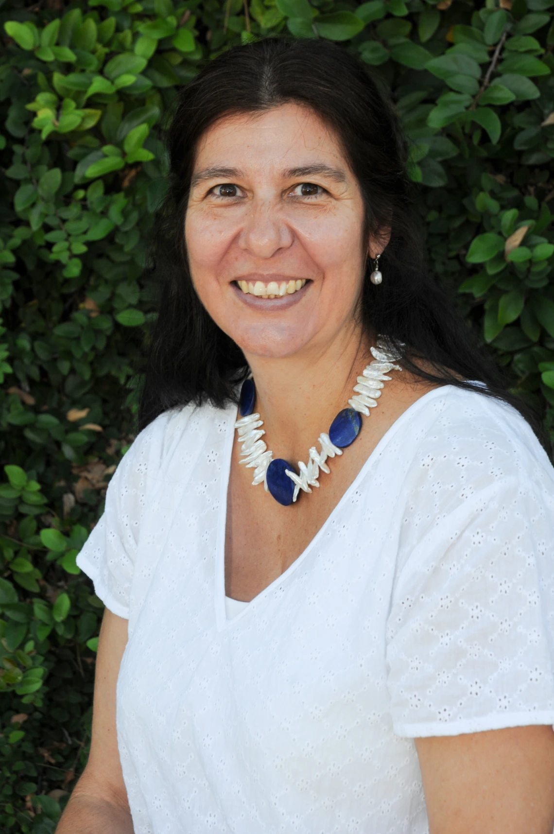 sara chavarria headshot, wearing a white blouse with greenery in the background