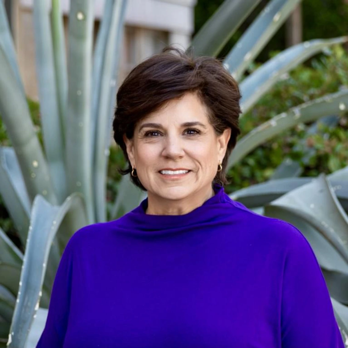 lydia crain headshot, short dark brown hair, wearing a purple blouse, standing outside with greenery in the background