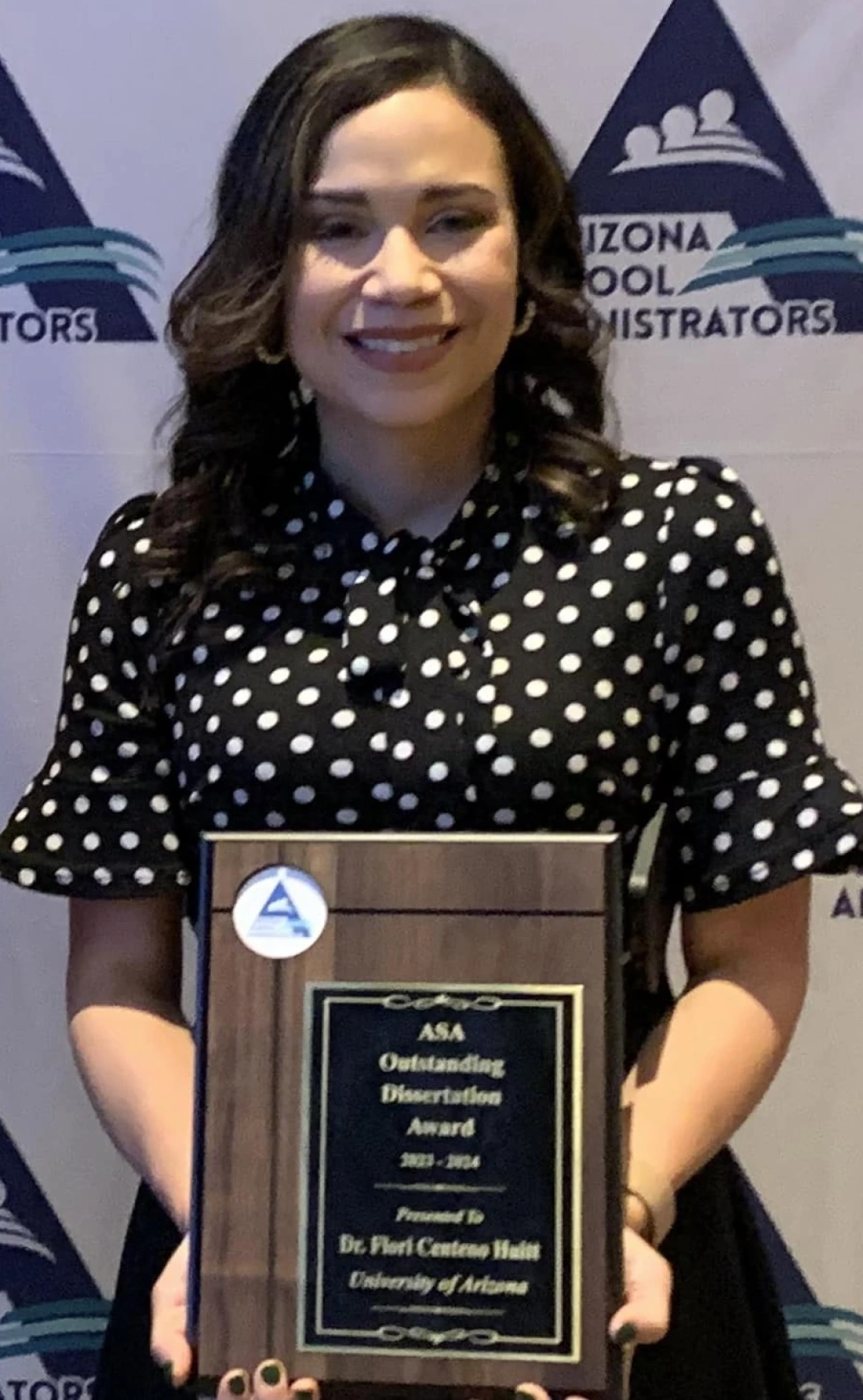 Flori Ceneno Huitt, wearing a polka dot black and white blouse, holding her award