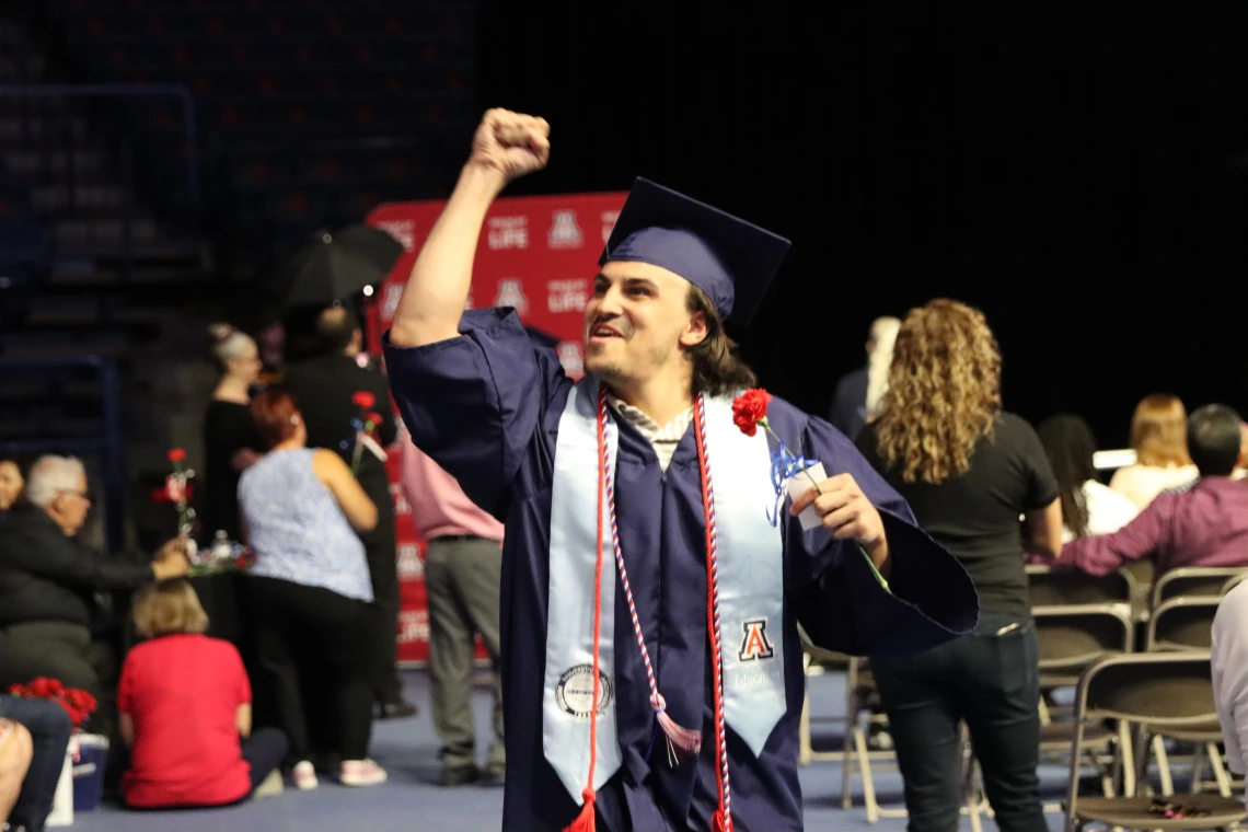 student walking in cap and gown during graduation ceremony fist pumping