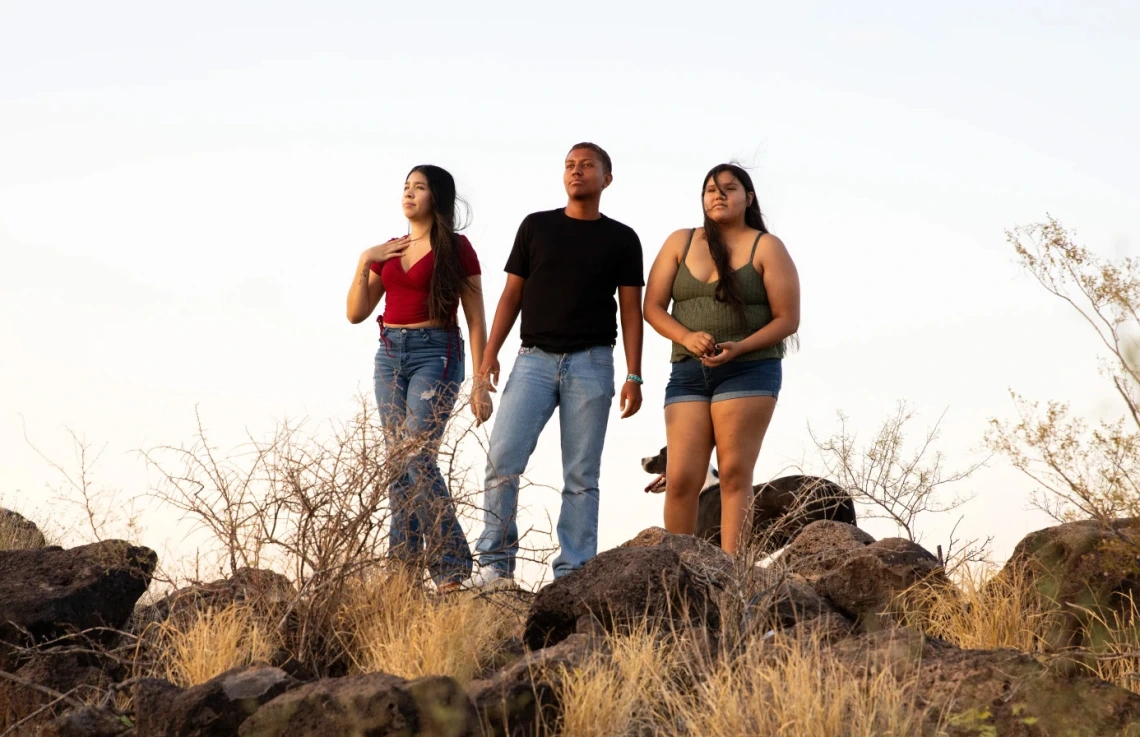 three young adults standing on a desert hilltop under a sunny sky