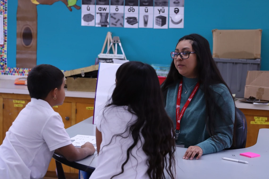 educator sitting at a table with two young students in a classroom