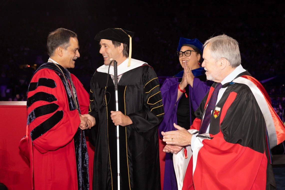 At a University of Arizona commencement ceremony, four distinguished individuals in academic regalia are gathered on stage.